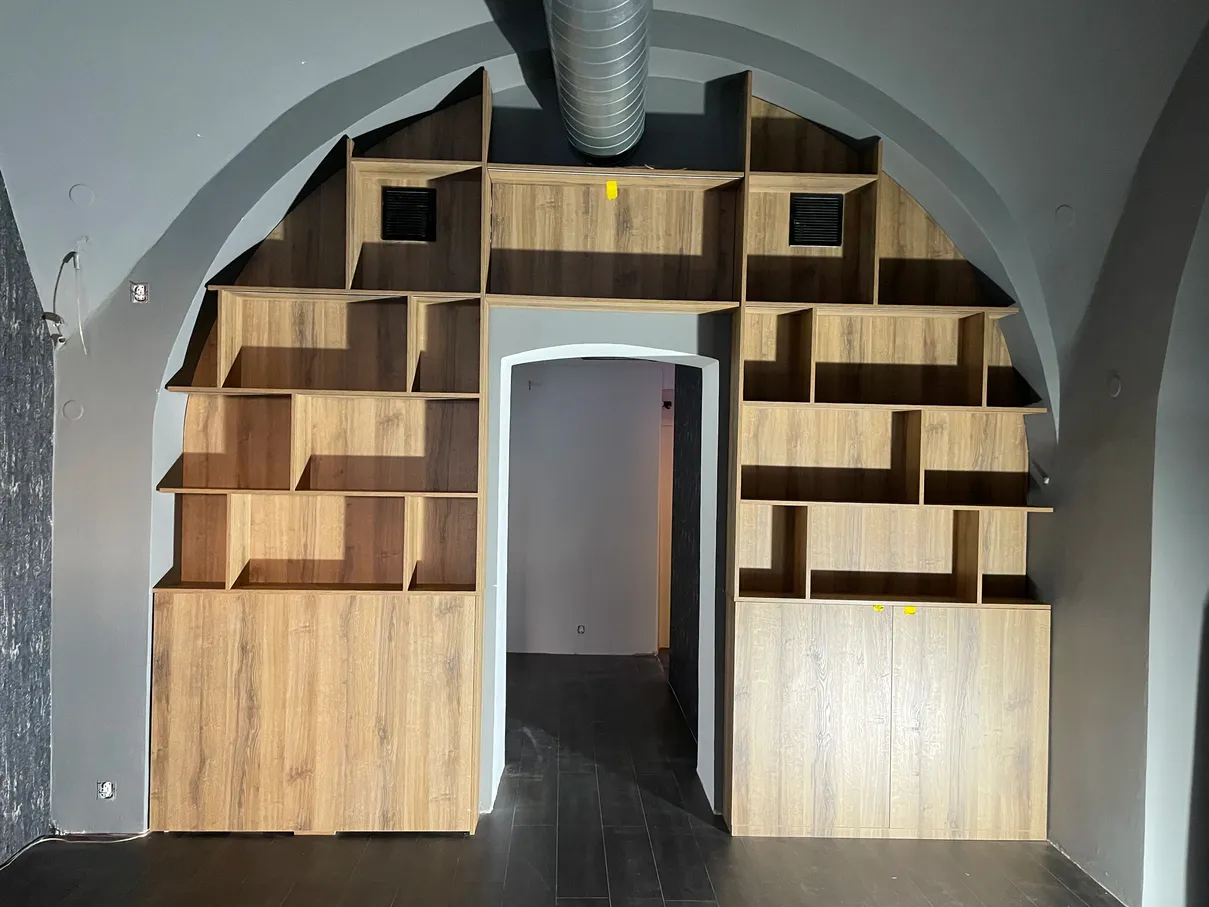 dřevěná knihovna s atypickými policemi vložená do obloku stropu místnosti
